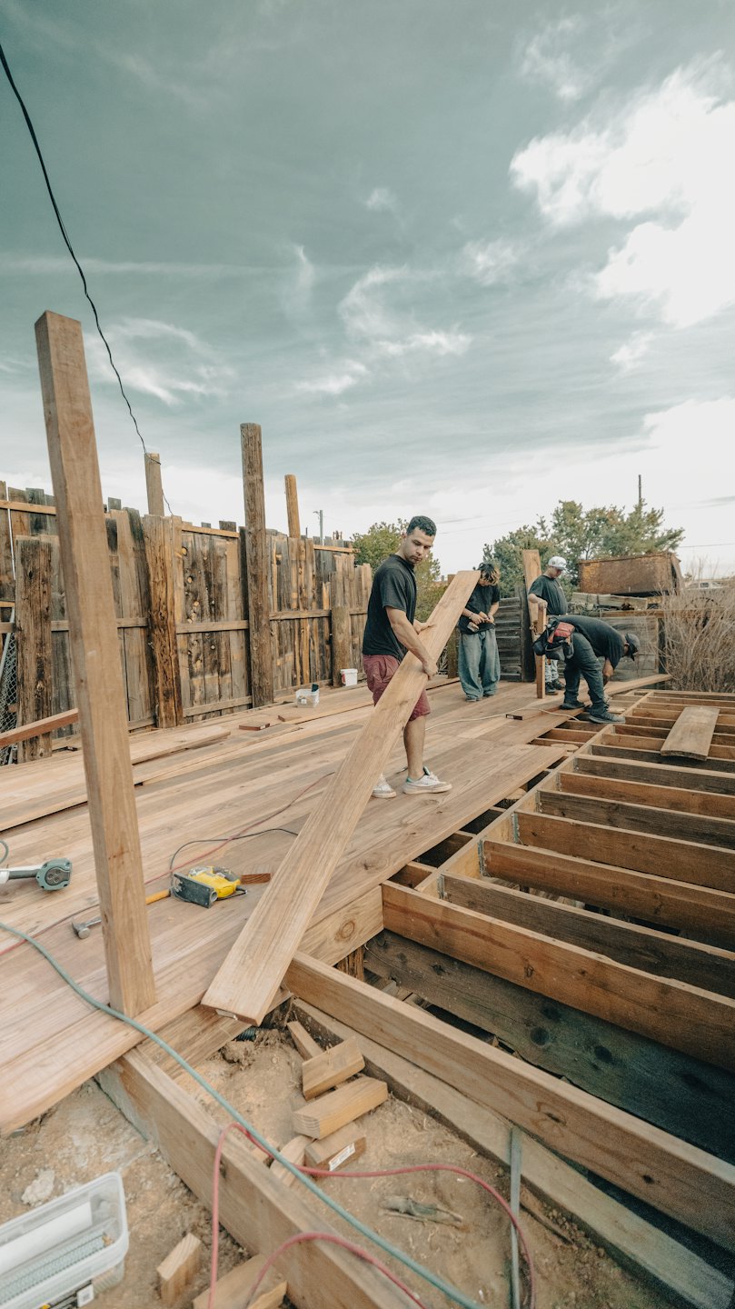 Construction workers build a large wooden deck outdoors.