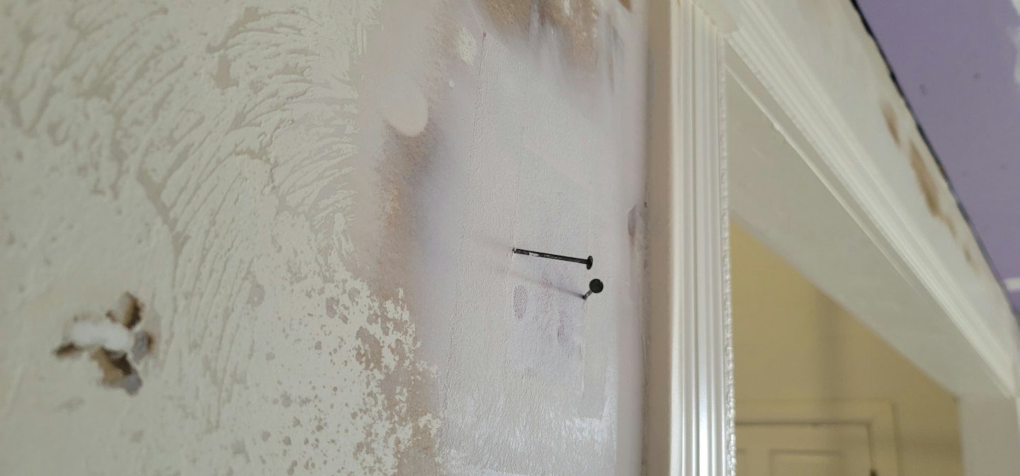 An interior wall with patches of fresh primer and protruding nails.