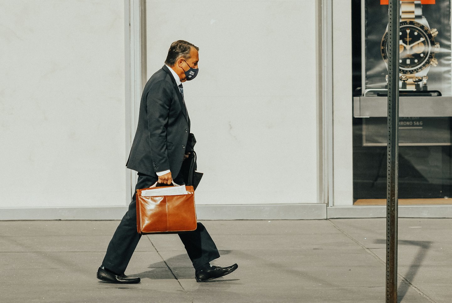 A man in a suit and mask carries a briefcase outside.