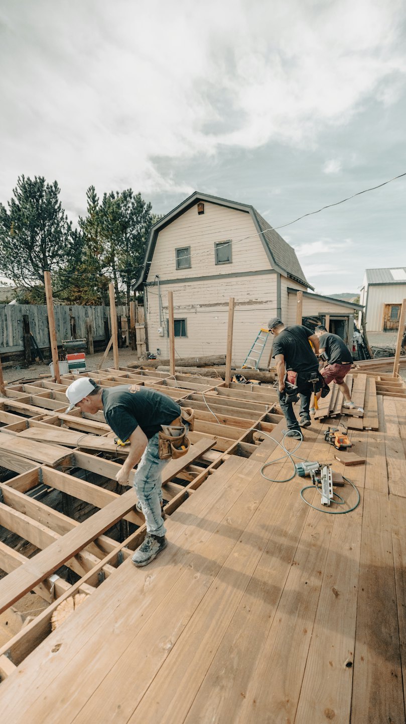 Men building a wooden deck frame with tools.